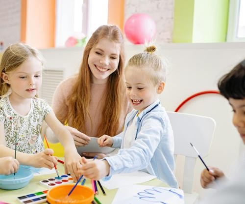Erzieherin mit Kindern an einem Tisch. Kinder malen mit Farben