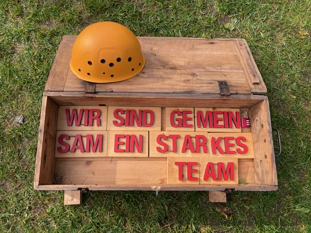 Eine Holzbox mit Buchstaben "Wir sind ein starkes Team" auf einer Wiese