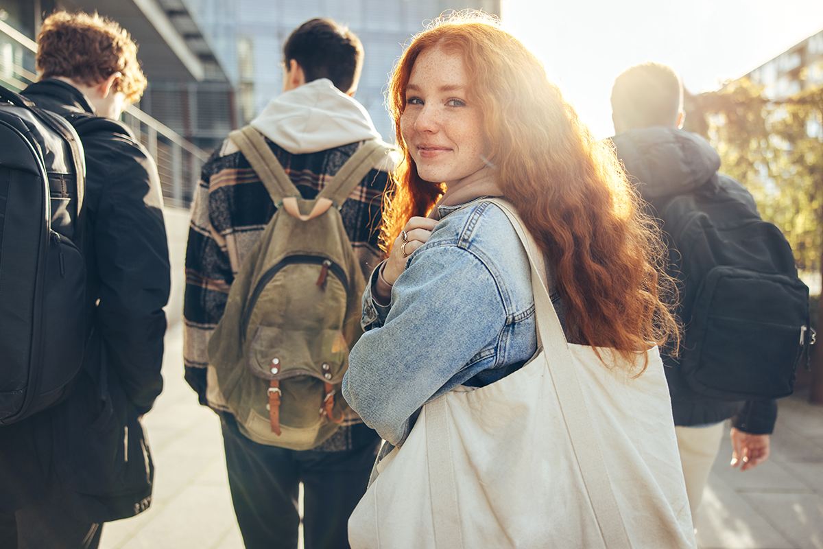 Schülerin blickt lächelnd zurück auf einem Schulcampus