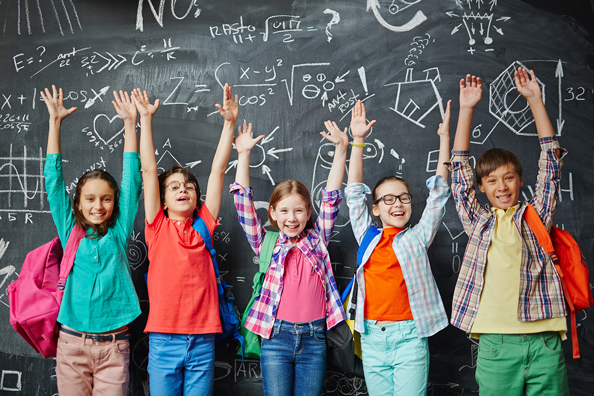 Junge Schülerinnen und Schüler vor einer Tafel mit erhobenen Händen