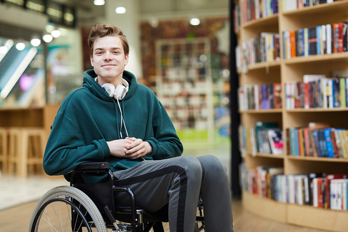 Ein junger Mann sitzend im Rollstuhl in einer Bibliothek
