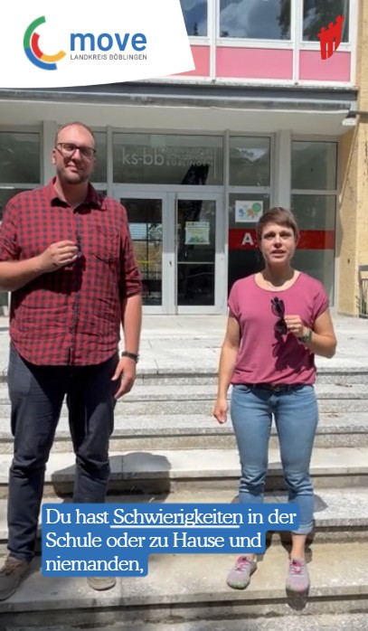 Zwei Personen vor einer Schule mit Mikrofon in der Hand