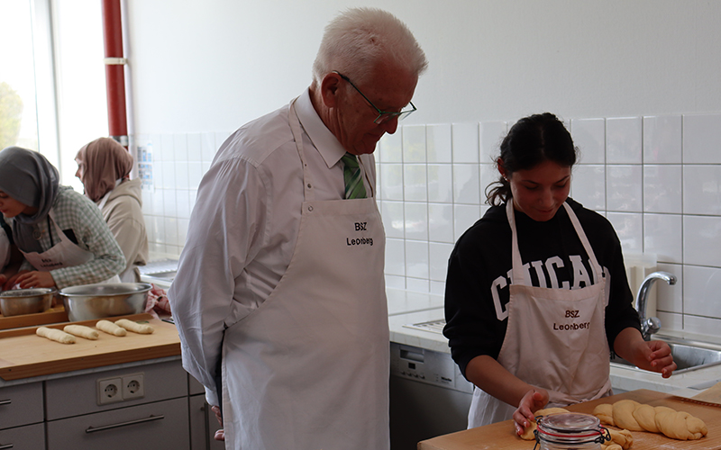 Herr Kretschmann neben einer Schülerin beim Hefezopfbacken in der Küche